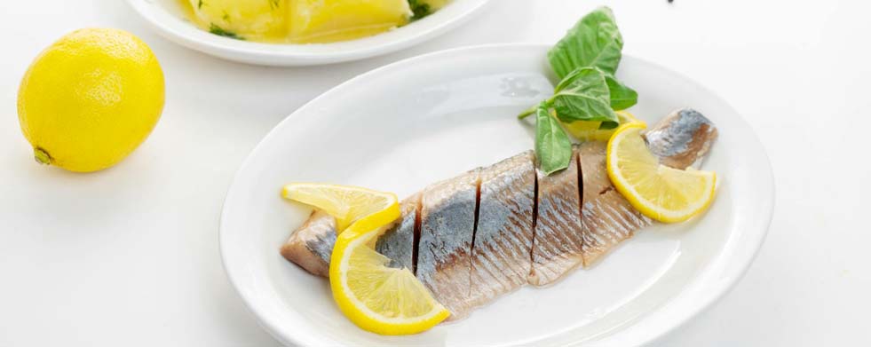 Zubereitetes Heringsfilet auf einem Teller, mit Salzkartoffeln als Beilage sowie Zitronenscheiben.